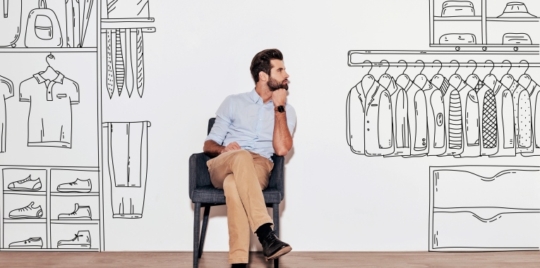Young handsome man keeping hand on chin and looking away while sitting in the chair against illustration of an organized closet in the background